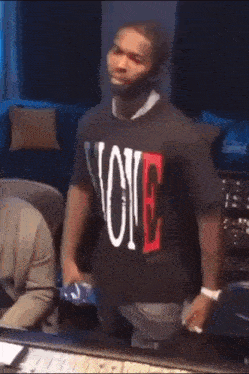 a man wearing a vlone shirt is standing in front of a keyboard .