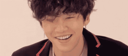 a young man with curly hair is smiling for the camera .