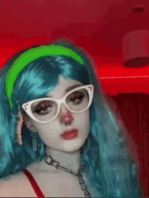 a woman with blue hair and glasses is wearing a clown costume and a green headband .