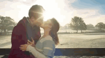 a man and a woman are kissing while sitting on a bench in front of a field .