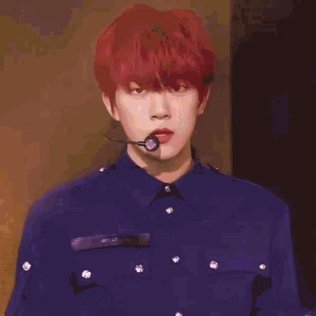 a young man with red hair and a microphone in his mouth is wearing a blue shirt .