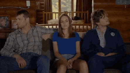 two men and a woman are sitting on a couch in front of a fireplace .