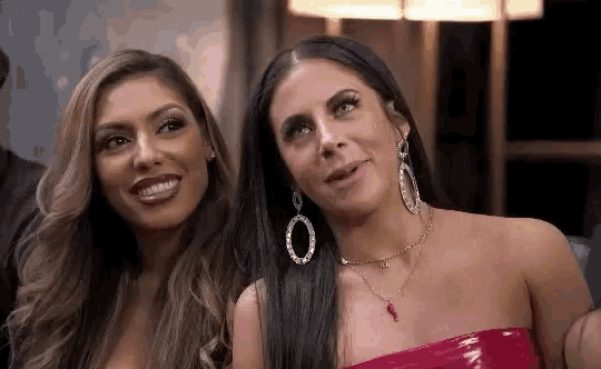 two women are sitting next to each other in a room and smiling .