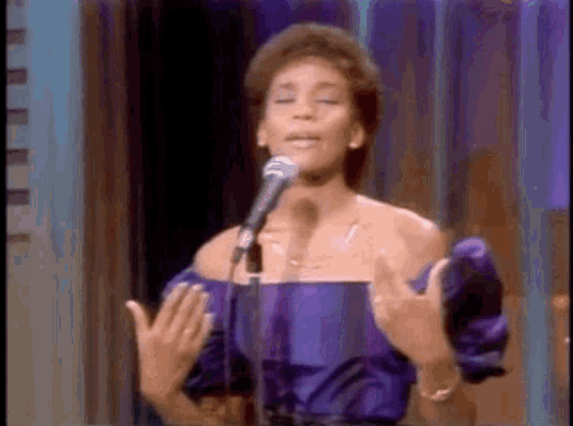 the woman is wearing a purple dress and singing into a microphone .