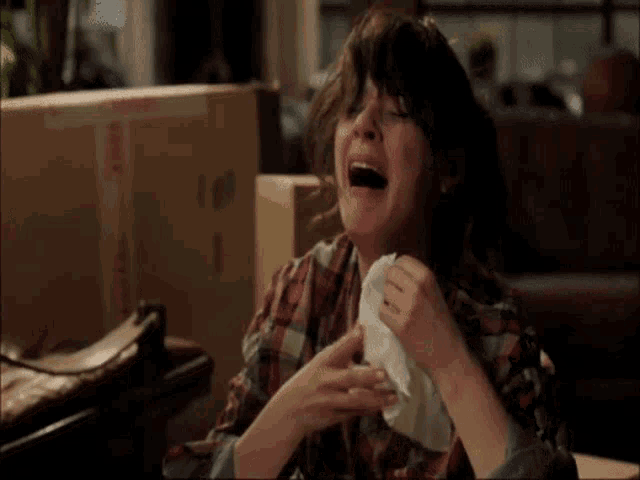 a woman in a plaid shirt is crying while holding a napkin in her hand .