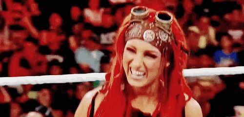 a woman with red hair and goggles on her head is making a funny face in a wrestling ring .