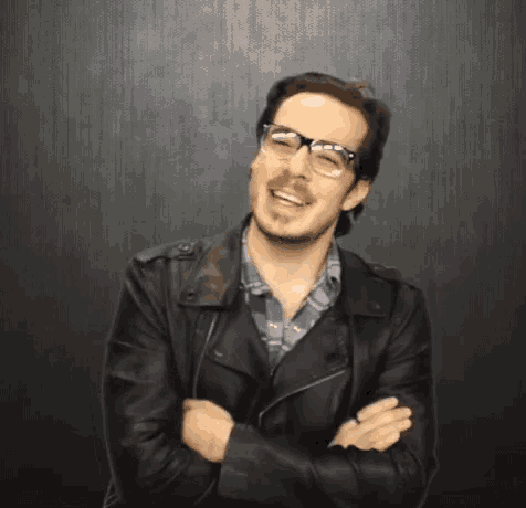 a man wearing glasses and a leather jacket is laughing .
