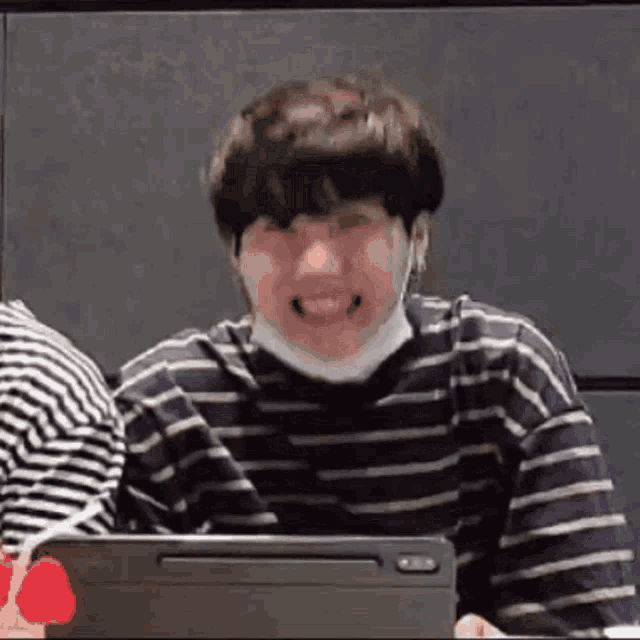 a man wearing a striped shirt is sitting in front of a laptop computer .