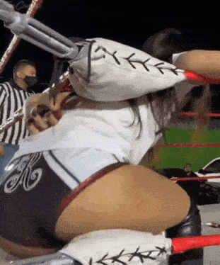 a woman is wrestling in a ring with a referee in the background .