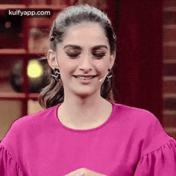 a woman in a pink shirt is smiling with her eyes closed while standing in front of a microphone .