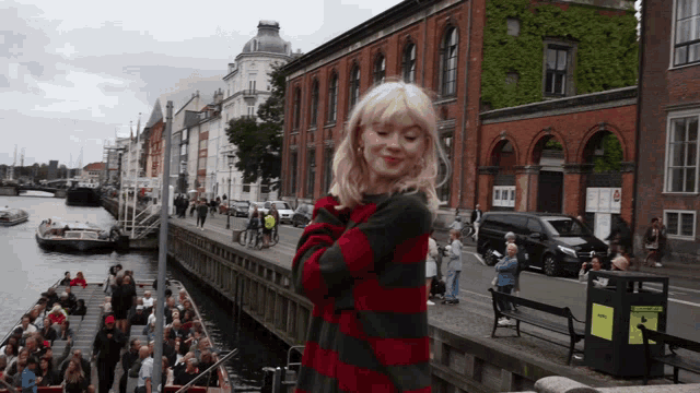 a woman in a red and black striped sweater stands on a bridge overlooking a body of water