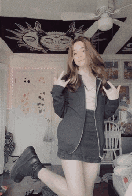 a girl wearing a black jacket and a black skirt stands in front of a ceiling fan