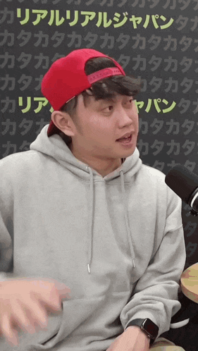 a man wearing a gray hoodie and a red hat with the word tokyo on it