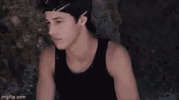 a young man wearing a black tank top and a black hat is sitting down .