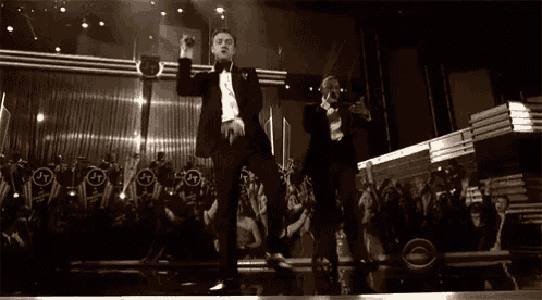 two men in tuxedos are dancing in front of a crowd