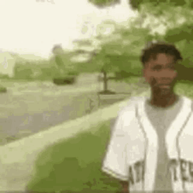 a man in a baseball uniform is standing on a sidewalk in front of trees .