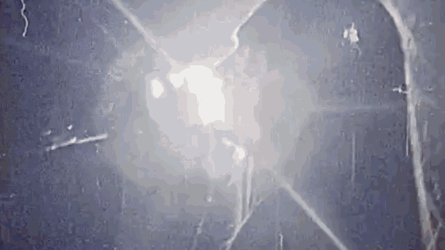 a close up of a broken glass window with a light coming out of it .