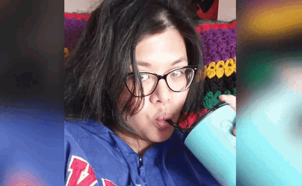 a woman wearing glasses is drinking from a cup with the letter v on it