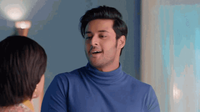 a man in a blue turtleneck is talking to a woman in a yellow dress