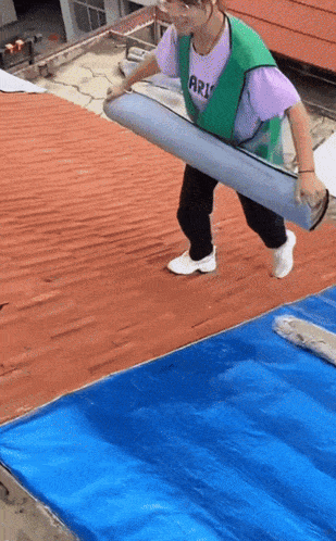a woman wearing a purple shirt that says arizona is carrying a roll of blue tarp