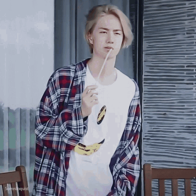 a man wearing a plaid shirt and a banana t-shirt is holding a straw in his mouth