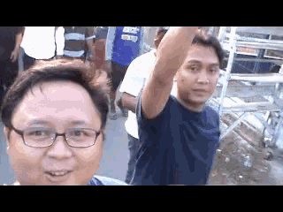 a man wearing glasses is taking a selfie with a group of people .
