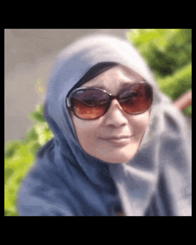a woman wearing sunglasses and a hijab is smiling