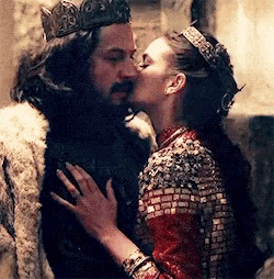 a man with a crown is kissing a woman in a red dress .