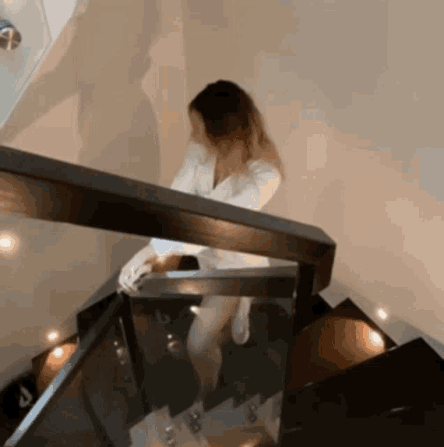 a woman is walking down a set of stairs with a glass railing