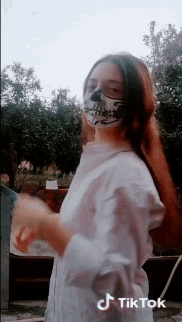 a woman wearing a mask with a skeleton face painted on it is dancing on a tiktok video