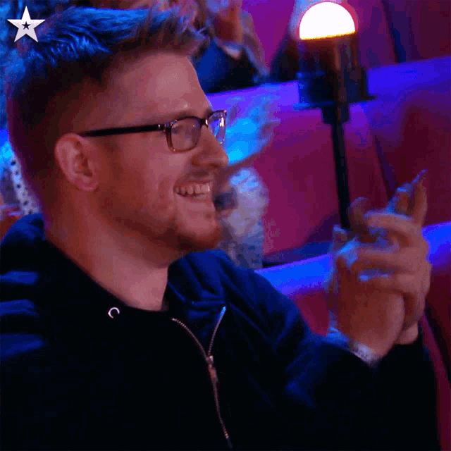 a man wearing glasses applauds in a dark room