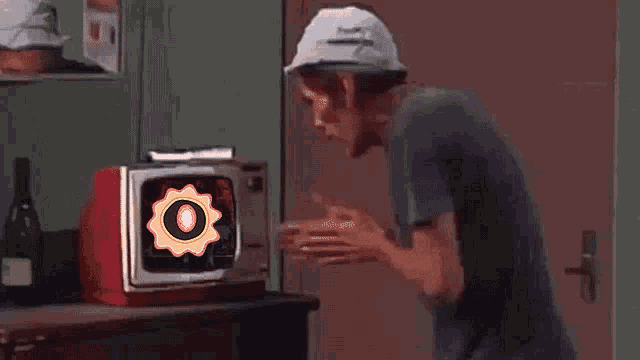 a man in a hat is standing in front of a television with an o on the screen
