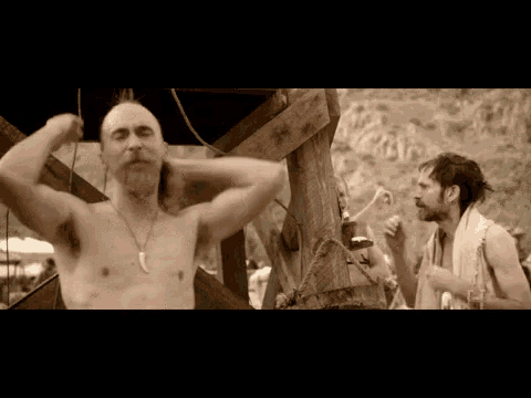 a man without a shirt is taking a shower while another man drinks beer