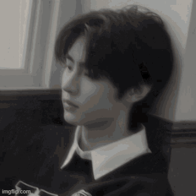 a black and white photo of a young man sitting in front of a window .
