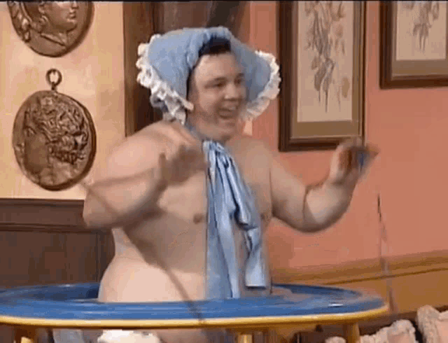 a shirtless man is standing in a baby bathtub wearing a blue hat and a blue towel .