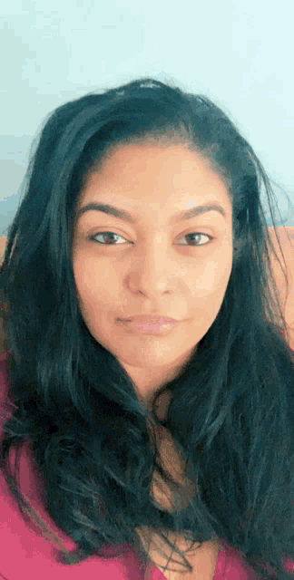 a woman with long dark hair and a pink shirt looks at the camera