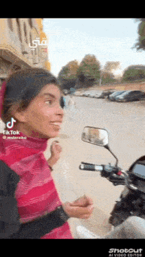 a woman is riding a motorcycle down a street and talking to a man .