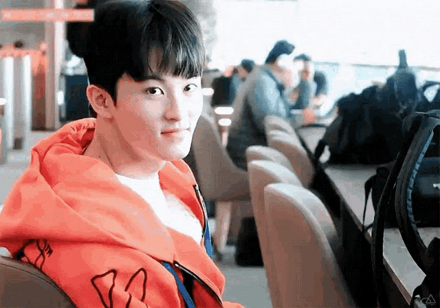 a young man wearing an orange hoodie is sitting in a chair looking at the camera .