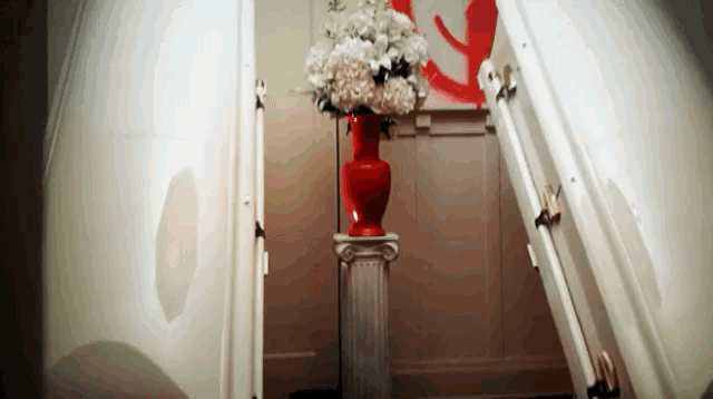a red vase filled with white flowers is on a pedestal