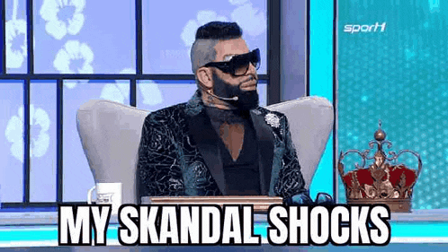 a man with a beard and sunglasses is sitting in a chair with a microphone in his mouth .