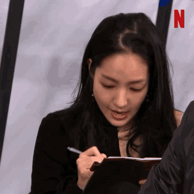 a woman is writing on a piece of paper with a pen in her hand .