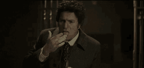 a man in a suit and tie is standing in a dark room and talking to someone .