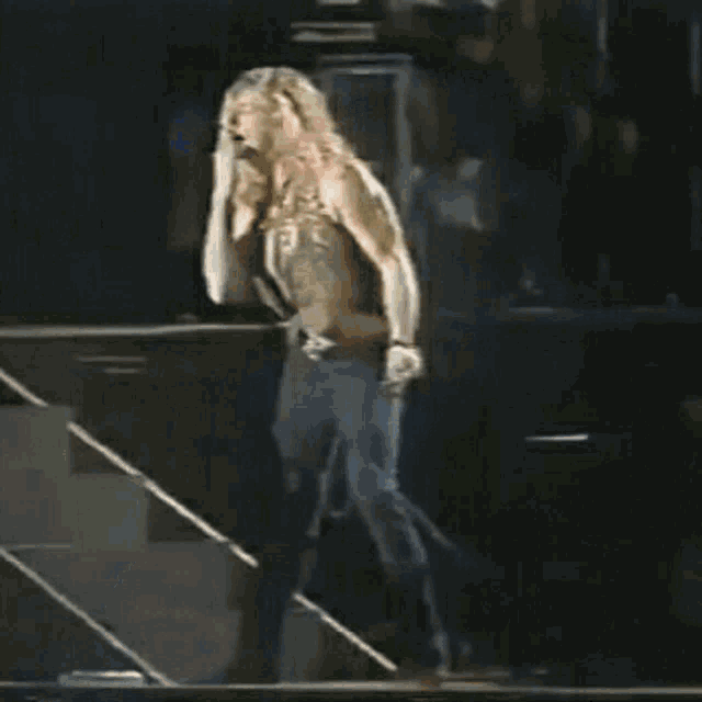 a man without a shirt is walking down stairs on a stage holding a microphone .