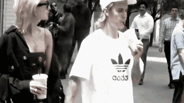 a man and a woman are walking down the street . the man is wearing a white adidas shirt .