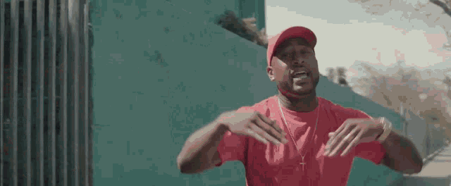 a man in a red shirt and red hat is standing in front of a green wall and making a funny face .