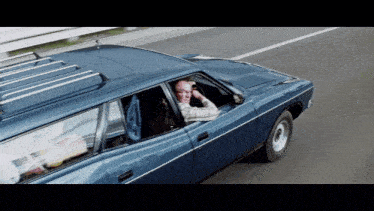 a man driving a blue car with a roof rack on it