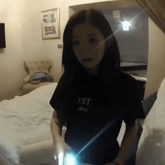 a woman wearing a black shirt that says just jean is standing in front of a bed