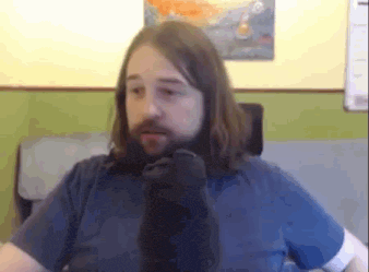 a man with long hair and a beard is sitting in front of a wall with a painting on it .