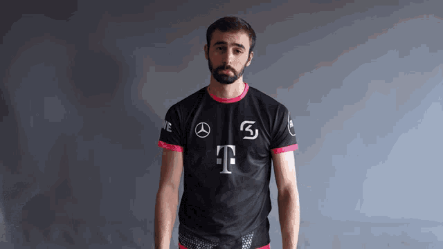 a man with a beard is wearing a black and pink shirt with the letter t on the front