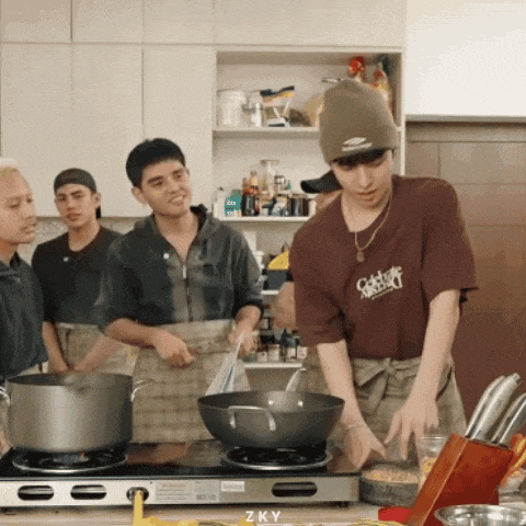 a man wearing a brown shirt that says zky is cooking in a kitchen
